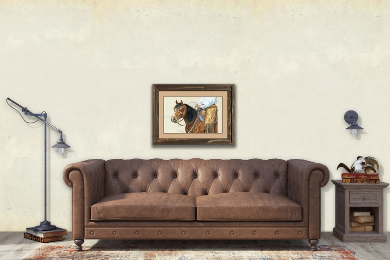 Peut inclure: Une peinture encadr&eacute;e &agrave; l'aquarelle repr&eacute;sentant un cow-boy &agrave; cheval, avec un cadre en bois marron. L'&oelig;uvre est affich&eacute;e au-dessus d'un canap&eacute; en cuir marron. La pi&egrave;ce a une esth&eacute;tique vintage, avec un lampadaire et une table d'appoint.