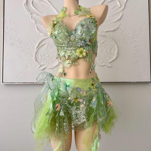 May include: A two-piece lime green outfit consisting of a halter-style crop top and a short skirt. Both pieces are heavily embellished with intricate lace, floral appliqués, sequins, and beads. The skirt features layered tulle and organza fabric.
