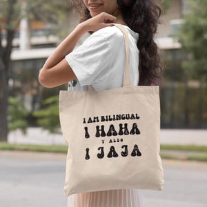 May include: A beige tote bag with black text that reads "I am bilingual I haha y also I jaja".