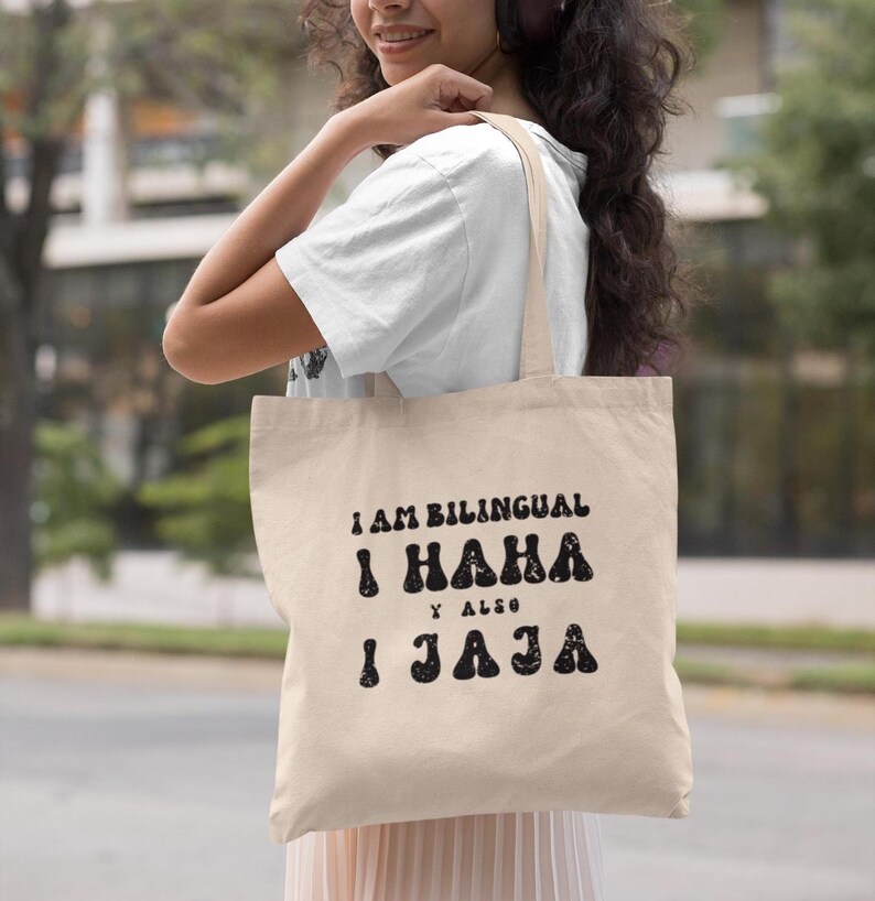 May include: A beige tote bag with black text that reads "I am bilingual I haha y also I jaja".