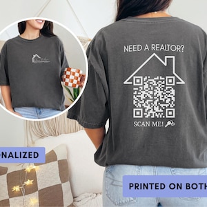 May include: Dark gray t-shirt with a house outline and text on the front. The back of the shirt features a house outline with a QR code and the text "Need a Realtor? Scan Me!" The shirt is printed on both sides.