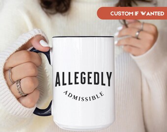 May include: White ceramic mug with a black rim and handle. The mug features the words "ALLEGEDLY" above "ADMISSIBLE" in black text. The mug is held by a person wearing a white sweater.