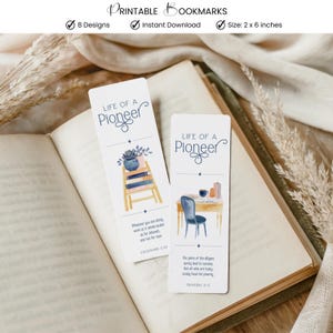 May include: Two white bookmarks with the text "LIFE OF A Pioneer" and watercolour illustrations. One shows a ladder with books and a plant, the other a desk with a chair. The bookmarks are 5 x 15 cm.