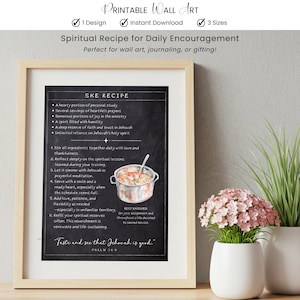 May include: A framed print with the text "Spiritual Recipe for Daily Encouragement." The black chalkboard-style print features a recipe with ingredients and instructions, along with a watercolor illustration of a pot of food. The print is in a light wood frame.