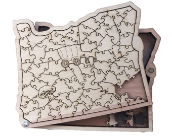 Op de afbeelding: Een houten puzzel van de staat Oregon met een wagen en een bever. De puzzelstukjes passen in een houten doos in de vorm van de staat Oregon.