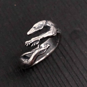 May include: A silver ring featuring a stylised design of two greyhounds intertwined. The ring is made of metal and has a smooth, polished finish.