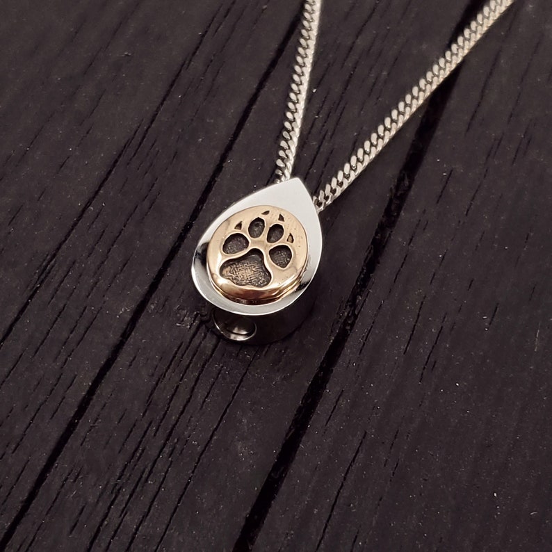 My dog track cremation urn pendant is made of hypoallergenic stainless steel with a mirror finish. Mounted on the front is my tiny solid bronze paw print. A discreetly placed screw can be removed from the bottom.