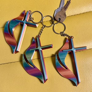 May include: Three iridescent keychains with a flame and cross design. The keychains are attached to a silver chain and a silver key ring.