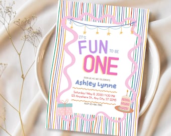 Op de afbeelding: Een rechthoekige verjaardagsuitnodiging met een kleurrijke verticaal gestreepte achtergrond en een golvende roze rand. De tekst luidt IT'S FUN TO BE ONE, JOIN US AS WE CELEBRATE ASHLEY LYNNE, Saturday 1 May 8, 2030, 4:30 PM, 123 Anywhere St., Any City, ST 12345, RSVP 123-456-7890. Het bevat een illustratie van een cadeau en een taart.
