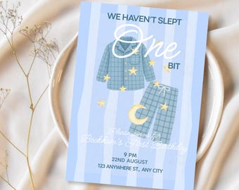 Op de afbeelding: Een rechthoekige verjaardagsuitnodiging met een lichtblauwe en witte verticaal gestreepte achtergrond. Het toont een blauwe pyjamaset met ruitjes, gele sterren en een halve maan. Tekst: WE HAVEN'T SLEPT One BIT, Please join us for Beckham's First Birthday, 9 PM, 22ND AUGUST, 123 ANYWHERE ST., ANY CITY.