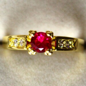 Könnte beinhalten: Ein goldener Ring mit einem roten Edelstein und kleineren weißen Edelsteinen auf der Ringschiene.