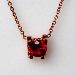 Op de afbeelding: Een delicate gouden ketting met een klein, rood edelsteen hanger.