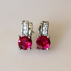May include: A pair of silver earrings with a single red gemstone and a row of smaller clear gemstones on each earring.