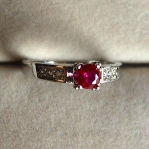 May include: A silver ring with a red gemstone and smaller white gemstones on the band.