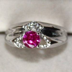 Può includere: Un anello d'argento con una pietra preziosa rosa circondata da piccole pietre bianche.