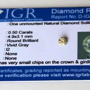 Könnte beinhalten: Ein Diamant-Gutachten der International Gemological Research Laboratories (IGR) für einen 0,50 Karat schweren, runden Brillanten in lebhaftem Grau. Die Berichtsnummer lautet D-IG-8299. Der Diamant weist sehr kleine Absplitterungen an Krone und Gürtel auf.