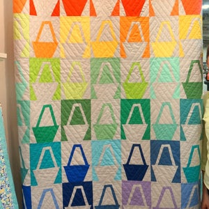 May include: A white quilt with a pattern of colourful baskets. The baskets are arranged in a grid pattern and are made of different colours, including pink, orange, yellow, green, blue, and purple.