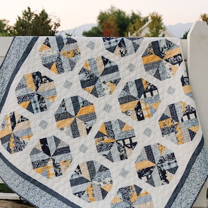 May include: A quilt featuring a repeating pattern of octagonal blocks in shades of navy blue, light blue, and mustard yellow, set against a white background. The text A Bushel and a Peck a pattern by AMY SMART Diary of a Quilter is visible.