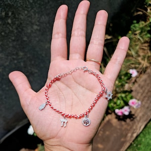 May include: A red string bracelet with silver charms, including a Star of David, a Tree of Life, and the Hebrew letter 'Chai'.