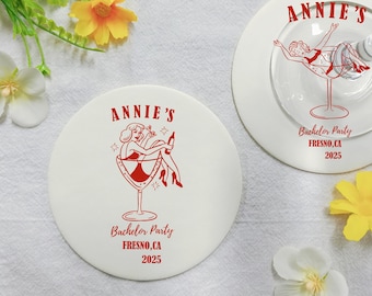 Può includere: Due sottobicchieri bianchi con grafica e testo rossi. Un sottobicchiere presenta una donna in un bicchiere da martini, l'altro un bicchiere da martini con una donna all'interno. Il testo recita "Annie's", "Bachelor Party" e "Fresno, CA 2025".