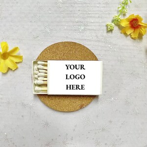 May include: A white box of matches with a cork coaster. The box has the text "YOUR LOGO HERE" printed on it.