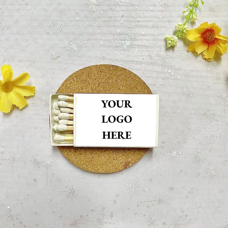 May include: A white box of matches with a cork coaster. The box has the text "YOUR LOGO HERE" printed on it.