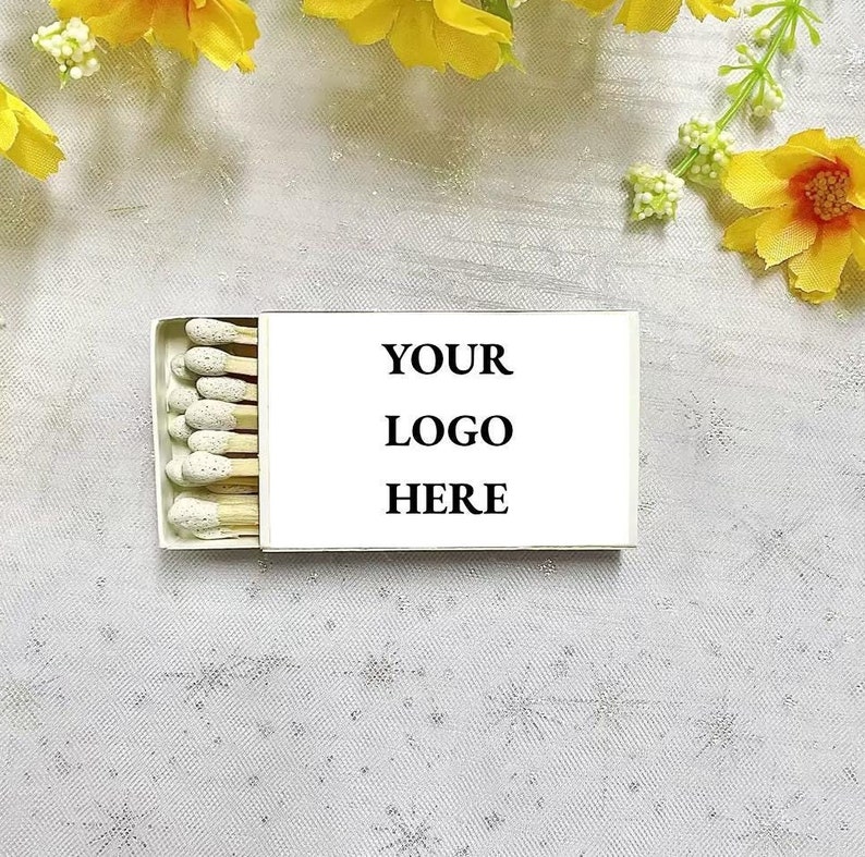 May include: A white box of matches with a white label that says "YOUR LOGO HERE". The box is on a white surface with yellow flowers.