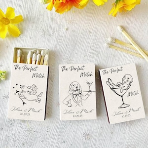 May include: Three matchboxes with the text "The Perfect Match" and the names "Jelina & Mark" with the date "10.29.25". Each box features a different dog illustration. One shows a dog as Cupid, another as a waiter, and the last in a martini glass.