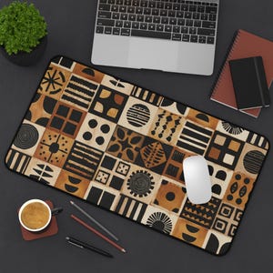 Puede incluir: Una alfombrilla de escritorio rectangular que presenta una cuadrícula de azulejos cuadrados con varios patrones geométricos negros y bronceados, incluyendo círculos, rayas, cuadrados y formas abstractas, en un diseño repetitivo y terroso.