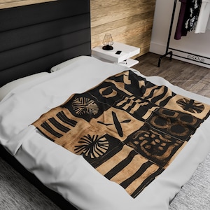 Könnte beinhalten: Ein weißer Bettbezug mit einer schwarzen und braunen gemusterten Überwurfdecke mit geometrischen Formen und Mustern. Die Decke hat einen tribalen oder ethnischen Charakter.