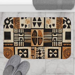 May include: A brown and black bath mat with a geometric pattern. The pattern features various shapes, including circles, squares, and triangles. The mat has a textured surface.