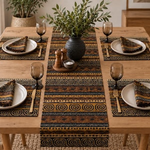 May include: A dining table setting featuring a table runner and four placemats with a repeating brown, black, and gold spiral and dotted pattern. Each place setting includes a white plate, a folded patterned napkin, a gold fork, and a gold knife.