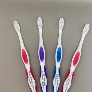 May include: Four white toothbrushes with personalized messages. The toothbrushes have red, blue, and purple accents. The messages include "Happy Birthday Lauren! Sweet 16!!!", "Ben and Jess November 12, 2024", "Matt's Going To Michigan! GO BLUE!!!", and "Steven Is Going To Alabama Roll Tide Roll!!!".