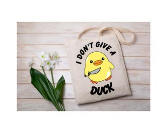May include: A white canvas tote bag with a yellow duck holding a knife and the text "I don't give a duck".