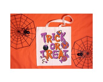 May include: White canvas tote bag with a purple and orange "Trick or Treat" design. The bag is on an orange background with black spiderwebs.