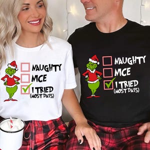 May include: White and black t-shirts with a Grinch graphic wearing a Santa hat and red coat. The text reads "NAUGHTY, MCE, I TRIED (MOST DAYS)" with check boxes. The shirts are paired with red and black plaid pajama pants.