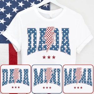 May include: White t-shirt with the word "DADA" in blue letters filled with white stars. A red and white checkered lightning bolt is in the center. Three red stars are below the word. Additional designs include "MINI" and "MAMA" in the same style.