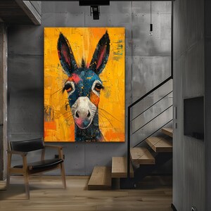 Op de afbeelding: Een kleurrijk abstract schilderij van een ezelskop tegen een gele achtergrond. De ezel heeft blauwe, zwarte, witte en oranje markeringen. Het schilderij hangt aan een muur in een modern huis.