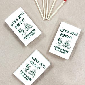 May include: White matchboxes with green text that reads "ALEX'S 30TH BEERDAY, CHEERS & BEERS TO 30 YEARS" are arranged with red-tipped matches. The design includes a grill and beer bottles. The background is a neutral beige.