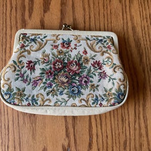 Op de afbeelding: Crèmekleurige vintage clutch met een bloemen tapestry design. De tapestry heeft een boeket van rode, roze, blauwe en gele bloemen met gouden accenten. De sluiting is goudkleurig.