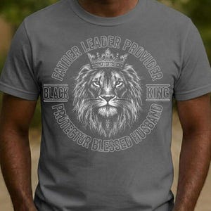 May include: Grey t-shirt with a detailed lion's head wearing a crown, encircled by text reading "Father Leader Provider King Protector Blessed Husband" and the word "Black".