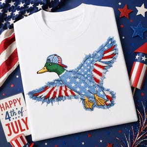 May include: White crew neck sweatshirt featuring an embroidered duck with wings designed in the style of the American flag. The duck wears a baseball cap with a matching flag design. The design is perfect for celebrating the 4th of July.