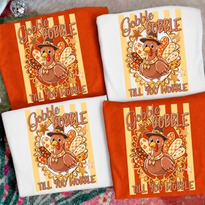 May include: Four t-shirts in orange and white featuring a graphic of a brown turkey wearing a hat. The design includes the text GOBBLE GOBBLE TILL YOU WOBBLE, surrounded by a decorative border of stars and autumn-colored patterned feathers.