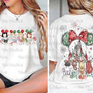 May include: White t-shirt featuring a watercolor design of Disney princesses with holiday-themed Minnie Mouse ears and candy canes. The back of the shirt shows a castle and fireworks with the text "Vibe Files Pick".