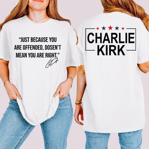 May include: White t-shirt with black text on the front that reads "JUST BECAUSE YOU ARE OFFENDED, DOSEN'T MEAN YOU ARE RIGHT." The back of the shirt has the name "CHARLIE KIRK" in a black box with red and blue stars.