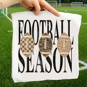 May include: A white t-shirt featuring the black distressed text FOOTBALL SEASON. Three football graphics are centered between the words, each with a unique pattern: a brown and tan checkerboard, a green and brown camouflage, and a tan leopard print.