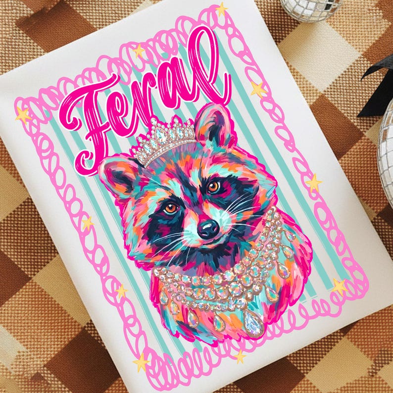 Pu&ograve; includere: Un cuscino decorativo quadrato bianco con un procione colorato con una corona e gioielli. La parola "Feral" &egrave; scritta in rosa sopra il procione. Lo sfondo ha strisce azzurre.