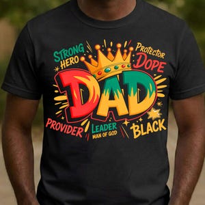Op de afbeelding: Zwart T-shirt met een kleurrijke afbeelding van "DAD" in grote letters, bekroond en omringd door woorden als "Strong", "Hero" en "Black". Een ideaal cadeau voor Vaderdag.