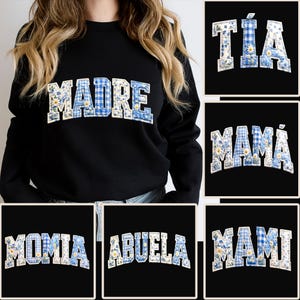 May include: Black sweatshirt featuring the word "MADRE" in large, blue and white floral and gingham patterned letters. Other images display "TÍA", "MAMÁ", "MOMIA", "ABUELA", and "MAMI" in a similar design.