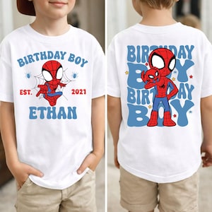 Może przedstawiać: Biały t-shirt z grafiką postaci z kreskówki Spider-Man. Z przodu znajduje się napis "BIRTHDAY BOY EST. 2021 ETHAN" w kolorze niebieskim i czerwonym. Z tyłu znajduje się duża grafika Spider-Mana z powtarzającym się niebieskim napisem "BIRTHDAY BOY".